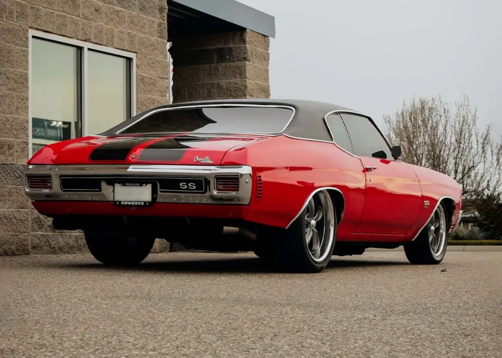 Picture of a red Chevrolet Chevelle with a brick house in the backfground