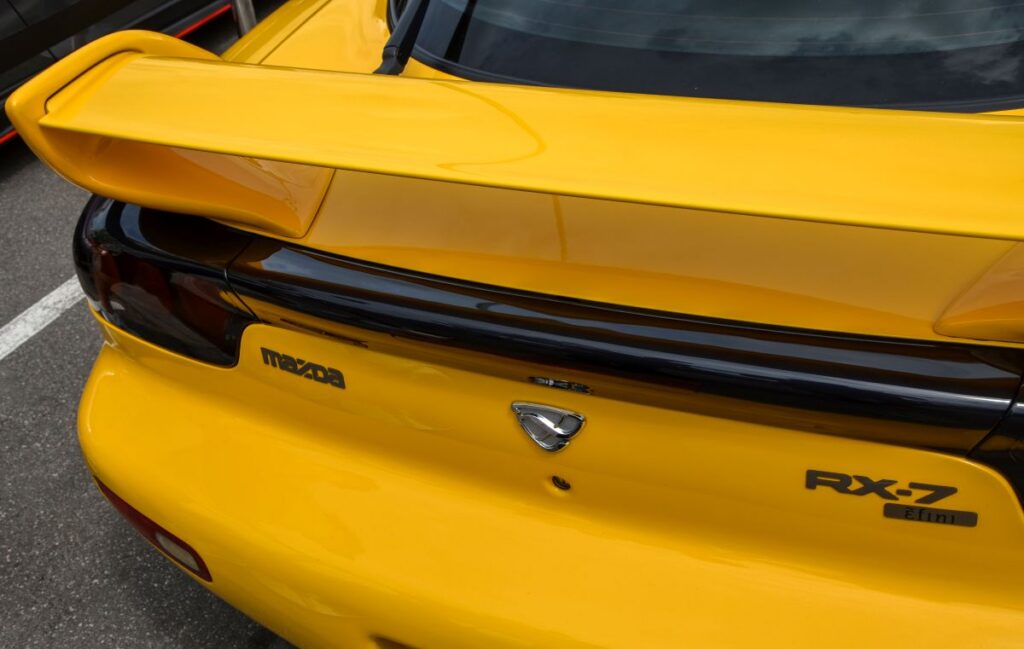 Detailed shot of the rear of a yellow Mazda RX-7 highlighting its classic design and distinctive spoiler
