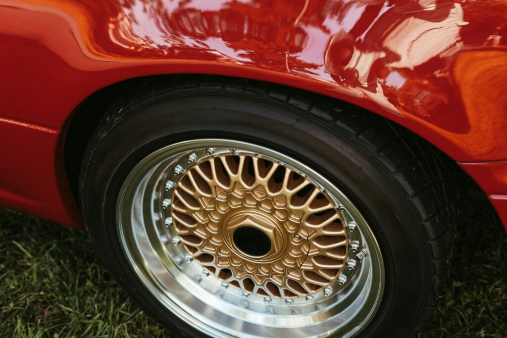 high-angle detail shot of a classic red sports car featuring a gold mesh-style multi-piece alloy wheel with a deep polished chrome lip
